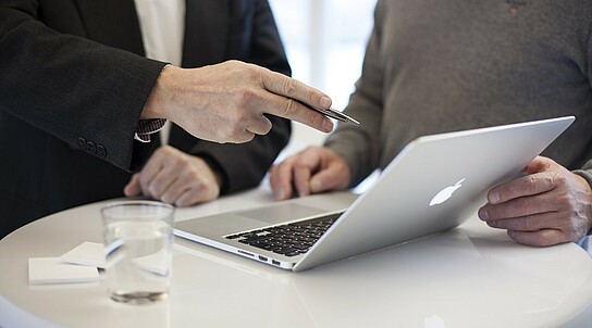 zwei Personen unterhalten sich während sie auf ein Laptop schauen